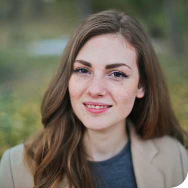 Amanda Lewis, a woman with long brown hair, smiles into the camera. She is wearing a tan blazer and a blue shirt.